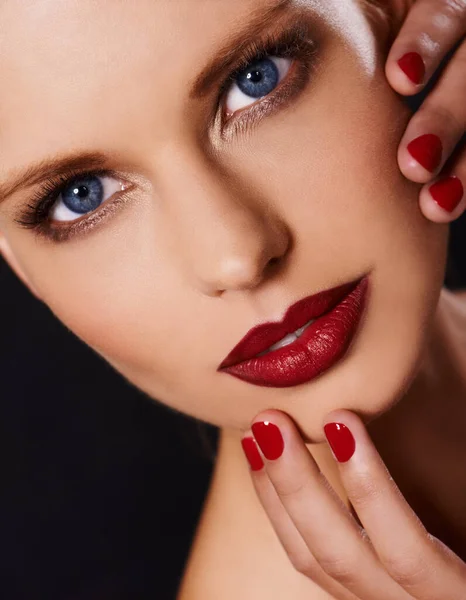 Make your lips match your fingers. Cropped image of a woman wearing red lipstick looking at the camera with fingers with red polish touching her face