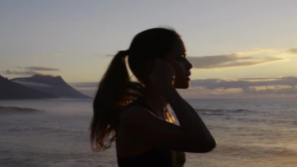 女性のシルエット ビーチと日没のランニング 運動とカーディオトレーニング 音楽のモチベーションと焦点 自由とフィットネスの健康目標 ランナー アスリート 海のワークアウト エネルギーとイヤフォンの影 — ストック動画