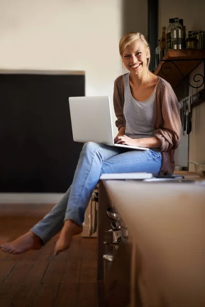 Kitchen写博客 一位年轻貌美的女士在厨房里轻松地使用笔记本电脑 — 图库照片