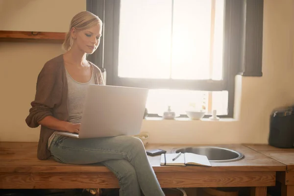 在网上找到完美的晚餐点子一位年轻貌美的女士坐在厨房柜台上用笔记本电脑 — 图库照片