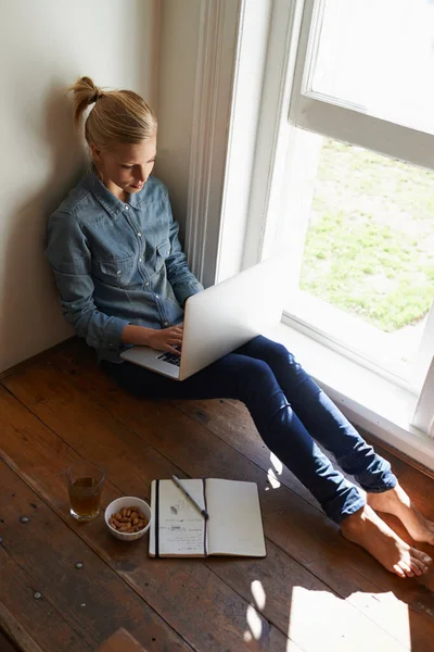 远离家里的喧嚣 一位年轻女子坐在窗边的地板上 在笔记本电脑上做一些研究 — 图库照片