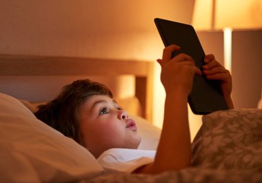 Yatma vakti geldi. Yatakta yatarken dijital tablet kullanan bir çocuk.