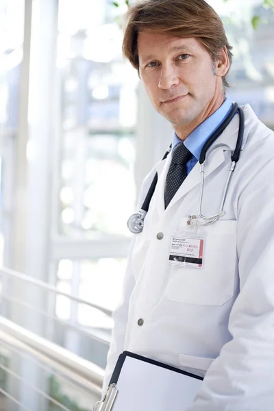 你有适当的健康保险吗 一位英俊的医生站在医院走廊上 手里拿着剪贴板 — 图库照片