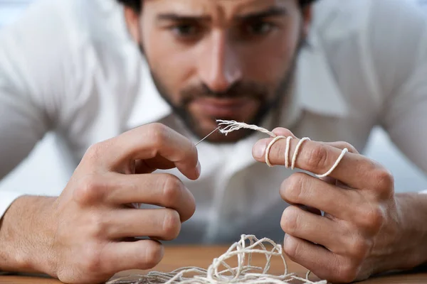 Threading a needle. A man struggling to thread string through a needles eye