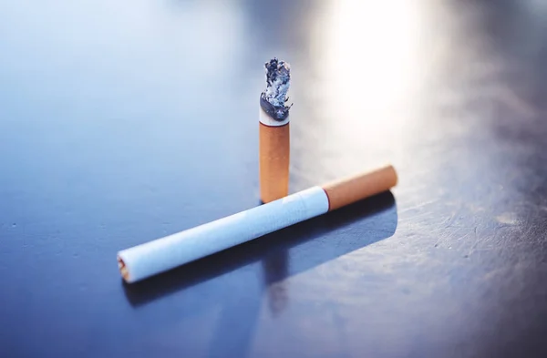 Smoking, tobacco and burning cigarette on table, close up of two cigarettes. Awareness for substance abuse, nicotine and unhealthy lifestyle addiction as cause for health issue, risk and lung cancer.