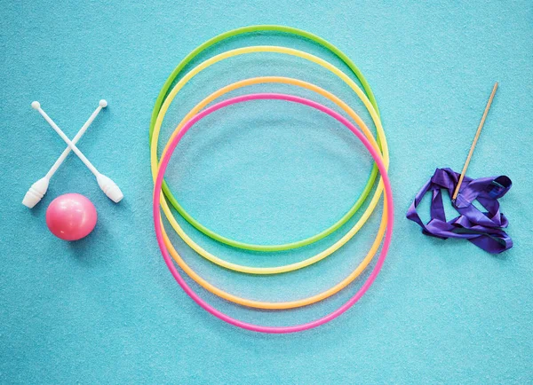 Gymnastics, dance and fitness with a hula hoop, ribbon and bars on an empty blue floor from above for exercise or training. Exercise, workout and still life with equipment for dancing or performance.