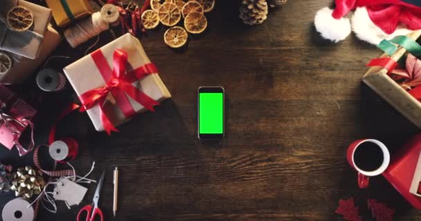 圣诞礼物或手持手机在绿色屏幕上进行营销 做广告或在桌上摆设产品 为网上购物节假日交易提供调校空间 促销或用户触摸移动设备 — 图库视频影像