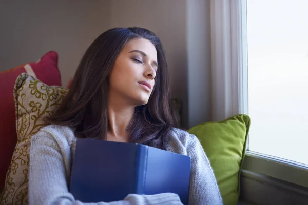 Relaxing with her favorite book. A young woman lying on the couch with a book