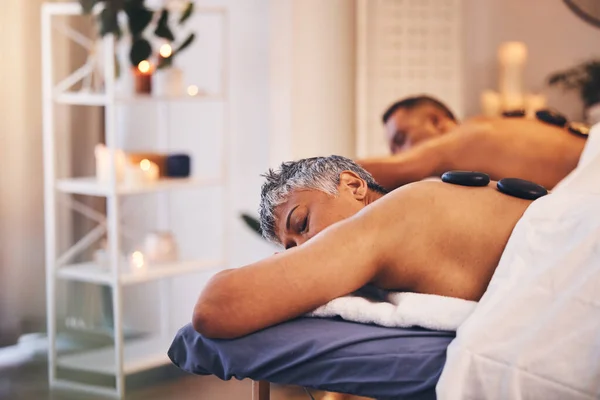 Relax, massage and hot stone with a couple in a spa, lying on a table or bed for physical therapy. Rock, sleep and luxury with a senior man and woman in a health or wellness center for stress relief.