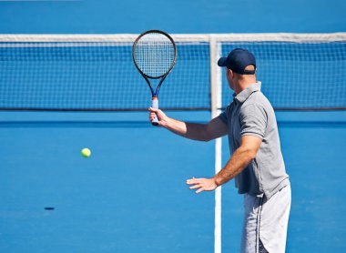 Her tenis antrenmanına geliyor. Tenis kortunda topu iade etmeye çalışan bir adam.