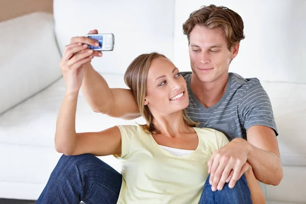 Making memories together. A young couple taking pictures with their cellphone in their livingroom