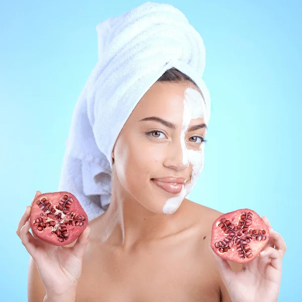 Beauty cream, face and woman with pomegranate, skincare and vitamin c for health, wellness and towel after shower in blue studio background. Model portrait, fruit and skin care, detox or clean facial.
