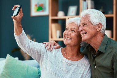 Bir çift, yaşlı, gülümseyen ve emekliliği olan bir selfie bir erkekle fotoğraf çektirmek için akıllı telefon tutan ve evinde mutlu bir kadın. Bağ, bağlılık ve evlilik, son sınıfların mutluluğu telefonlu fotoğraflarda.