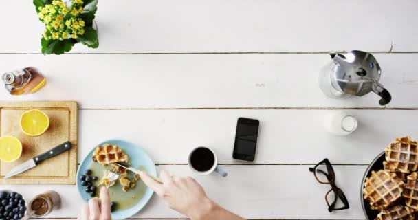 早餐和洒咖啡的电话与水果 华夫饼和食物在家里的桌子的顶部 早上在智能手机上用手 茶和凌乱的液体来吃蓝莓 柠檬和健康饮食 — 图库视频影像