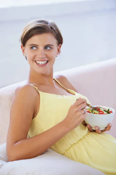 彼女の赤ちゃんのための健康的な食事療法の利点 ソファに座っている間に健康的なサラダを楽しんでいるリラックスした妊婦 — ストック写真