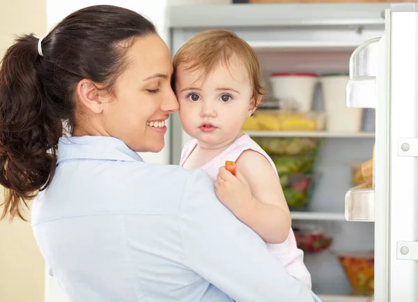 She can be fussy sometimes. a cute baby being held by its caring mom in front of an open fridge