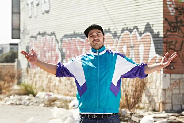 Cool and with attitude. A gangster standing in front of a graffiti wall with his arms outstretched