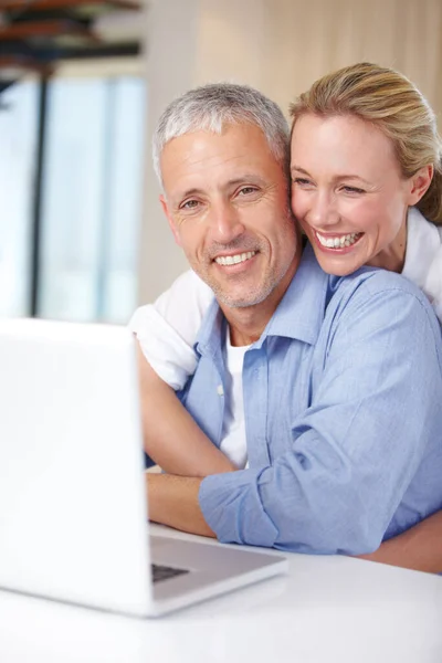 Hows it going. A woman hugging her husband as he works on the laptop at home