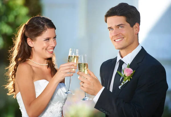 Toasting the new couple. Portrait of two young newlyweds toasting with champagne and smiling at the camera