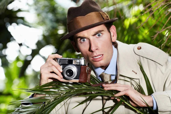 Oh no, Ive been spotted. Reporter taking a photo with a shocked expression from a thicket of bushes