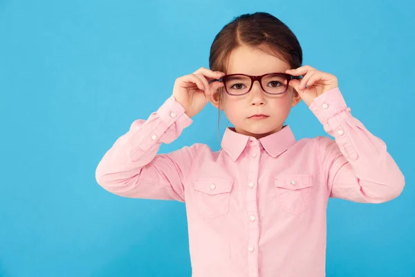 她非常聪明 一个严肃的小女孩拿着眼镜侧面的蓝色背景 — 图库照片