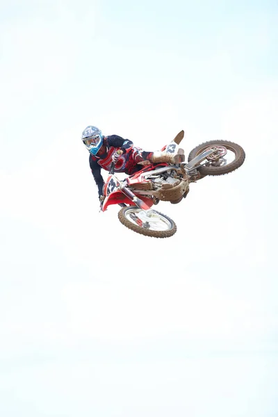 The definition of a daredevil. Low angle view of a motocross rider mid-air against a cloudy sky