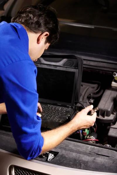 Running diagnostics. A male mechanic running electrical diagnostics on a car using a laptop