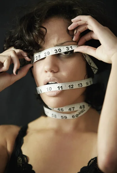 Obsessed with losing inches. Concept shot of an anorexic woman with measuring tape wrapped around her head