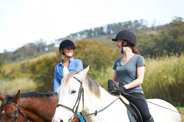 野外で馬に乗って楽しむ 乗馬中に二人の若い女性が話している — ストック写真