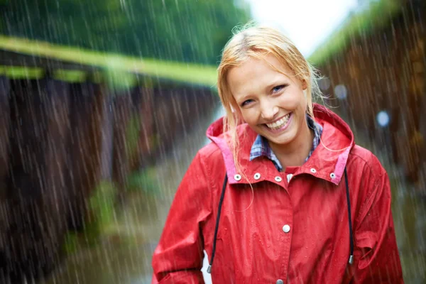 A little rain is quite nice. Gorgeous young blonde woman wearing a red raincoat in the rain outdoors on a country road