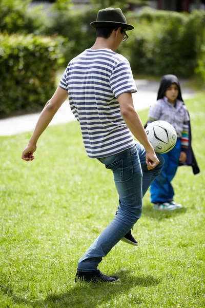 Enjoying a quick game - Soccer. Young guy playing football outdoors with a little girl in the background