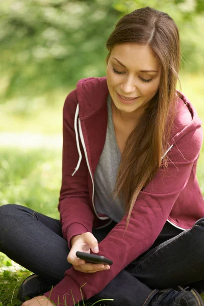 それを簡単に取る グリーンフィールドに座っている間 彼女の携帯電話にかなり若い女性のテキストメッセージ — ストック写真