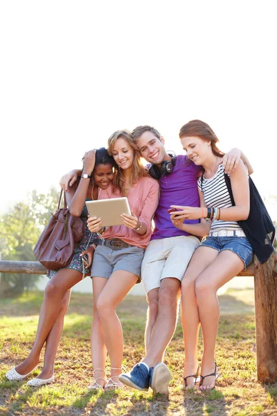 享受最好的技术和大自然可以提供的 四个朋友坐在外面分享音乐 通过触摸板上网 — 图库照片
