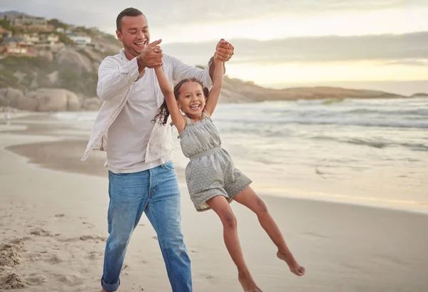 Cute little girl swinging while holding hands with her father. Young dad walking hand in hand with his daughter and lifting her while walking on the beach. Family fun in the summer at sunset.