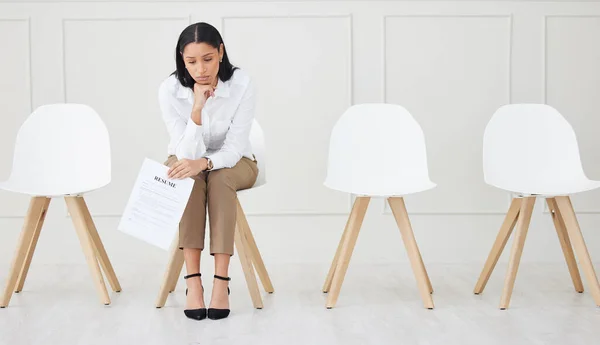 Full length of mixed race businesswoman waiting for interview. One young stressed applicant sitting alone. Sad ethnic professional holding resume in line for job opening, vacancy, office opportunity.