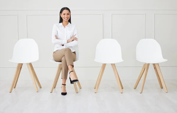 Full length of mixed race businesswoman waiting for an interview. One young applicant sitting alone. Professional candidate with arms folded in line for job opening, vacancy and opportunity in office.