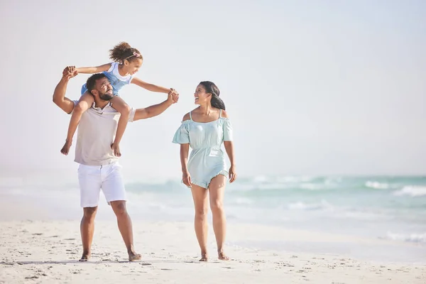 Full length of a happy mixed race family walking along the beach and enjoying vacation. Adorable little sitting on her fathers shoulders while enjoying family time by the beach with her two parents.