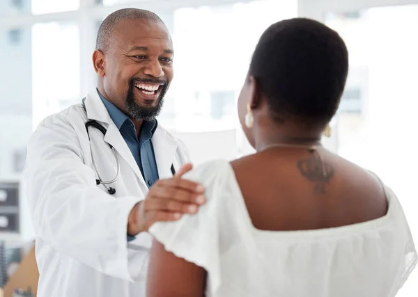 Cheerful doctor offering a patient support. Mature african american doctor touching a patient on the arm. Happy gp offering a patient comfort in a consult. Doctor talking to a patient.