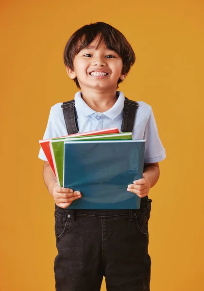 Portrait of a cute little asian boy wearing casual clothes while reading against an orange background. Happy and content while focused on education. Child holding a stack of books.