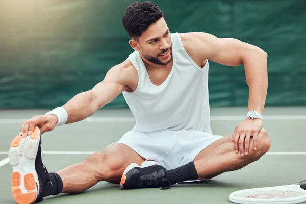 Full length smiling mixed race tennis player stretching legs and getting ready for court game. Hispanic fit athlete sitting alone and holding stretch as warmup before match. Sporty man in sports club.