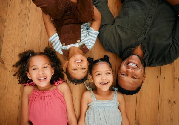 A happy mixed race family of four relaxing and lying on the lounge floor together. Loving black single parent bonding with his kids while being affectionate at home.