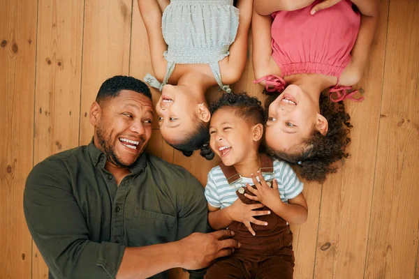 A happy mixed race family of four relaxing and lying on the lounge floor together. Loving black single parent bonding with his kids while being affectionate at home.