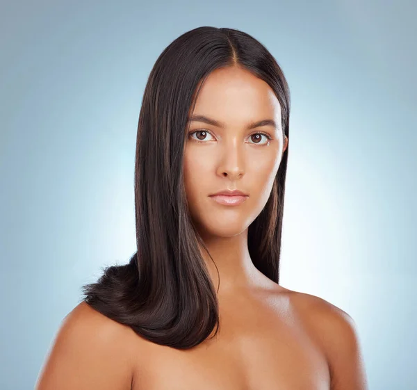 Portrait of a hispanic brunette woman with long lush beautiful hair posing against a grey studio background. Mixed race female standing showing her beautiful healthy hair.