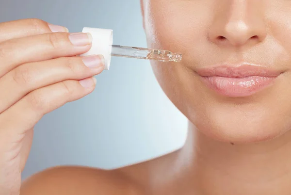 Closeup of an unknown woman using dropper to apply face serum to her lips. Caucasian model isolated against a grey background in a studio using skin oil for healthy glowing skin in skincare routine.