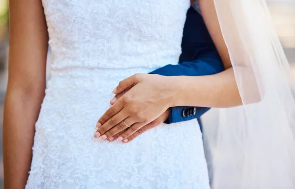 Close up of a bride and groom posing together. Woman placing her hand on her husbands as they stand together. Bride in beautiful white dress.