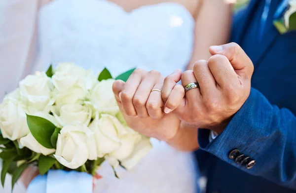 Closeup view showing hands of bride and groom couple on wedding day with ring bands on fingers. Newlyweds with pinky fingers interlocked making promise.