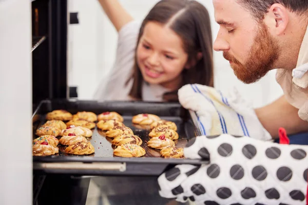 Father and daughter baking cookies at home. Parent taking baking tray with biscuits out the oven. Single dad and daughter preparing home bakery.