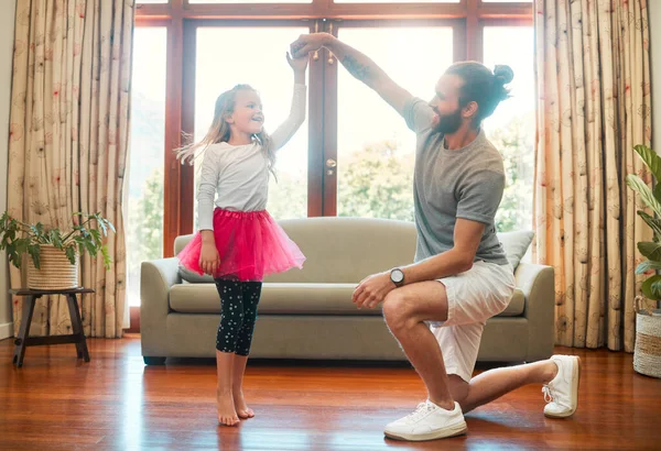 Young happy caucasian father and daughter dancing together in the lounge at home. Cute cheerful little girl practicing a dance with her dad. Father helping a child with a dance.