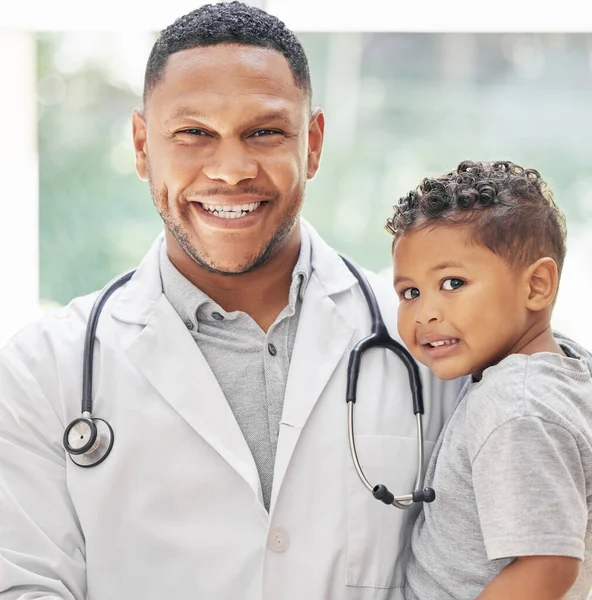 Portrait of handsome young black paediatrician holding adorable little boy in hands, cute child and doctor smiling during medical check up in clinic.
