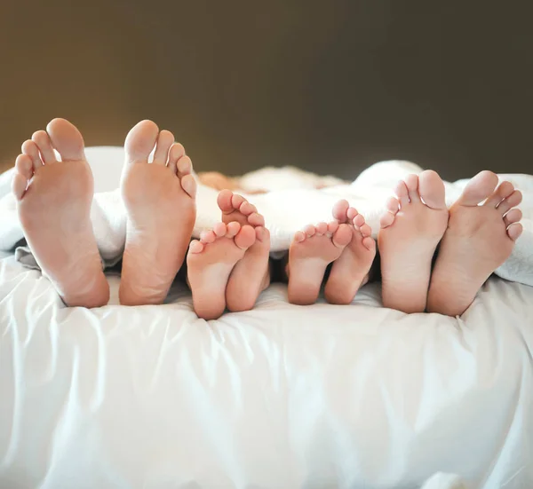 Comfy family lying in a bed together relaxing taking a nap together. Feet and toes of parents and their children being lazy and resting on a bed together during the day at home.